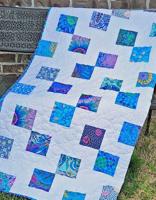 Double the Charm quilt pattern with sample quilt done in blue Kaffe Fassett charm squares on a white background.