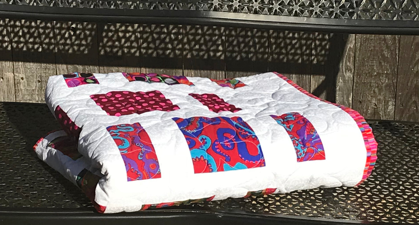 Quilt Pattern for charm squares that has nine columns of squares and rectangles with sashing between the columns. Quilt is displayed folded on a bench with colorful Kaffe Fassett fabrics.