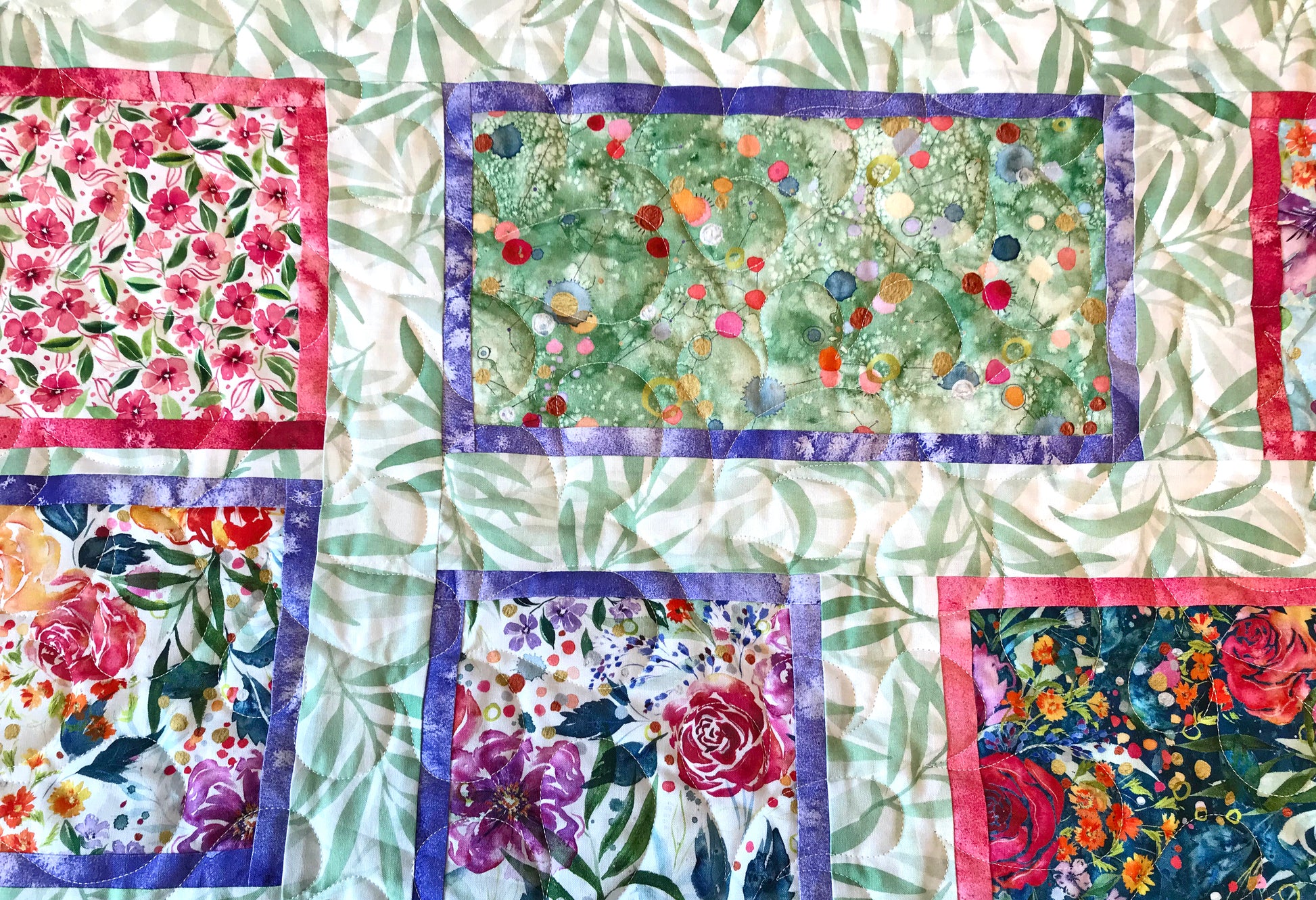 Close up of quilting on Handmade quilt featuring watercolor floral squares and rectangles framed with pink and purple fabric on a light green background.