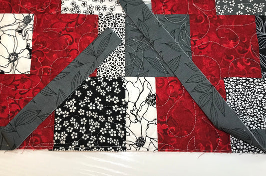 Red and gray patchwork quilt with two gray binding strips laying across it.