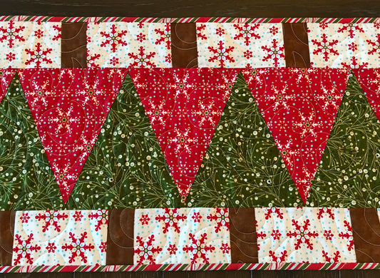 Close up of Christmas trees on handmade Christmas table runner with Christmas tree wedges and brown trunks surrounded by a tan border and green binding.