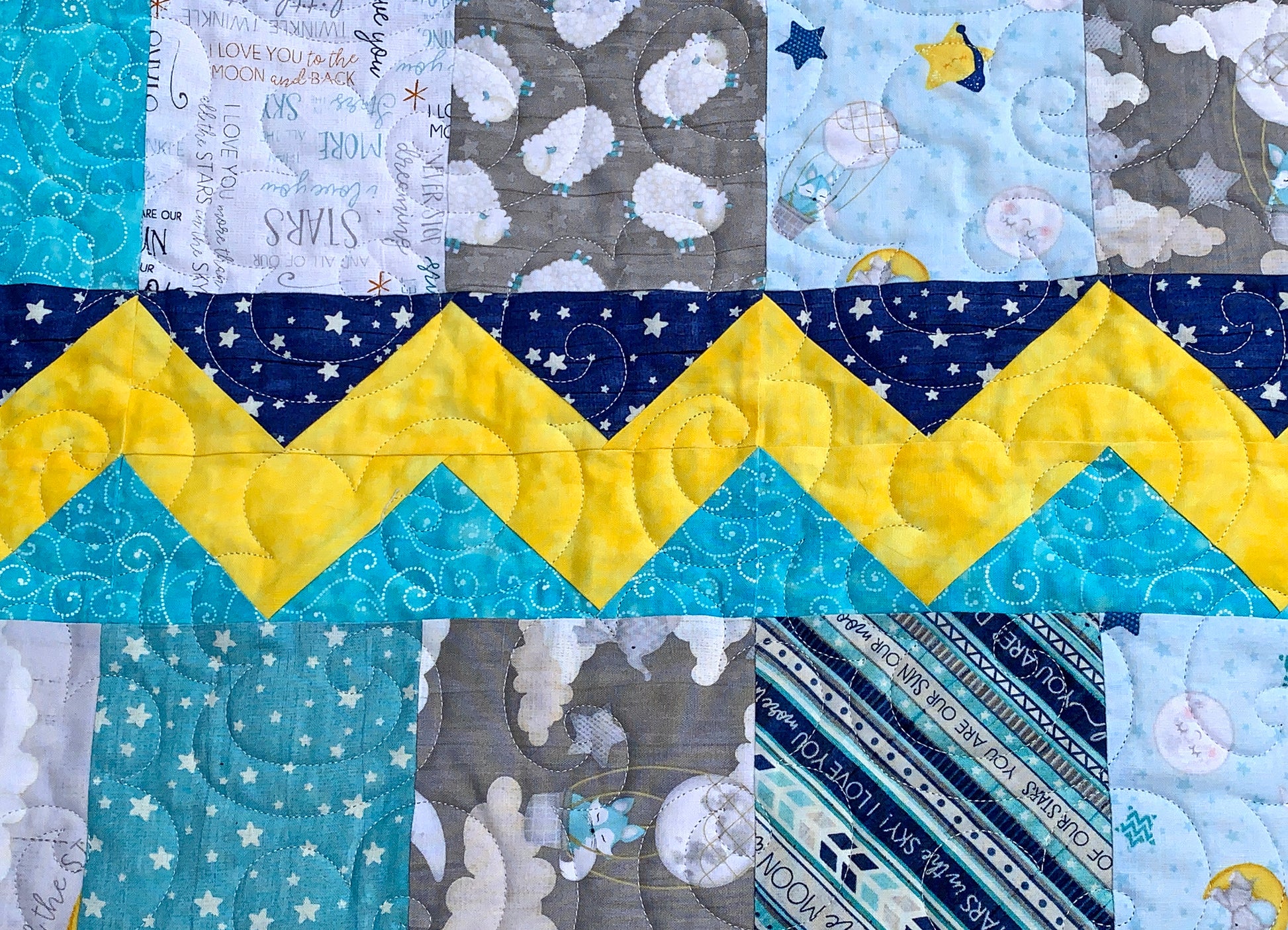 Close up of quilting on blue, yellow, teal and gray patchwork baby or toddler quilt with four zig-zag rows accenting the patchwork blocks.