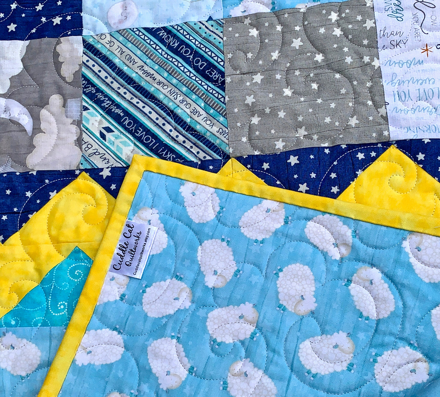 Close up of corner label on blue, yellow, teal and gray patchwork baby or toddler quilt with four zig-zag rows accenting the patchwork blocks.