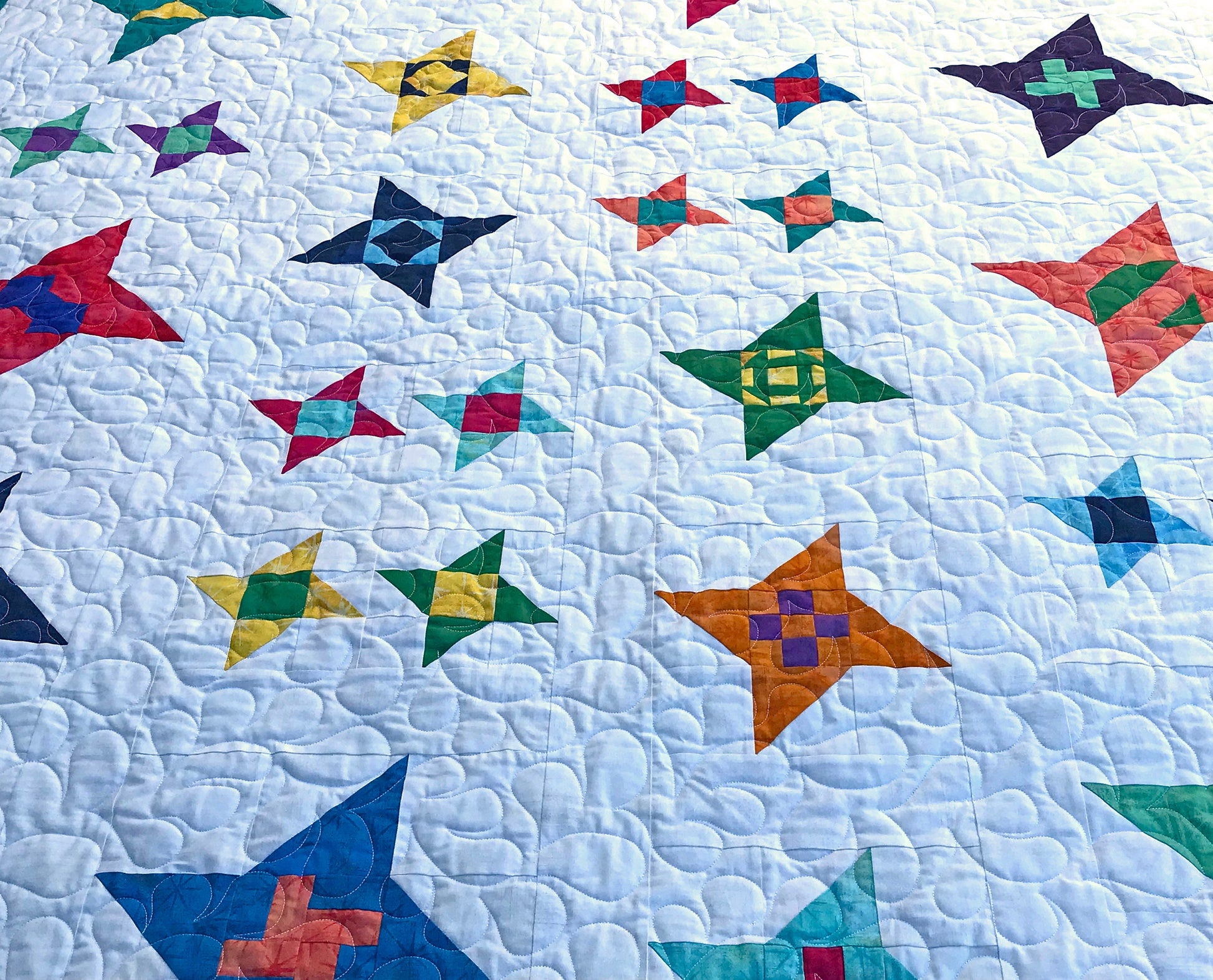 Close up of feather quilting on Star Gazing modern star sampler quilt pattern sample quilt. Stars are in various sizes with various fabrics on a white background.