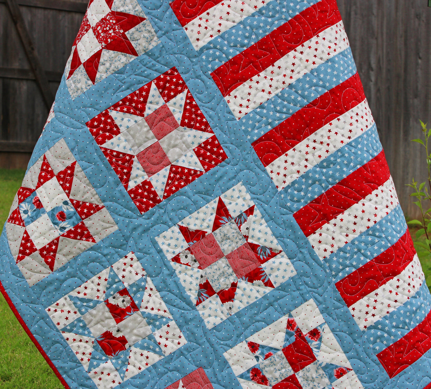 One Nation patriotic quilt pattern sample quilt with patchwork stars in three sizes and red white and blue stripes and blue sashing. Quilt is shown hanging on a tree with close up of the stars.