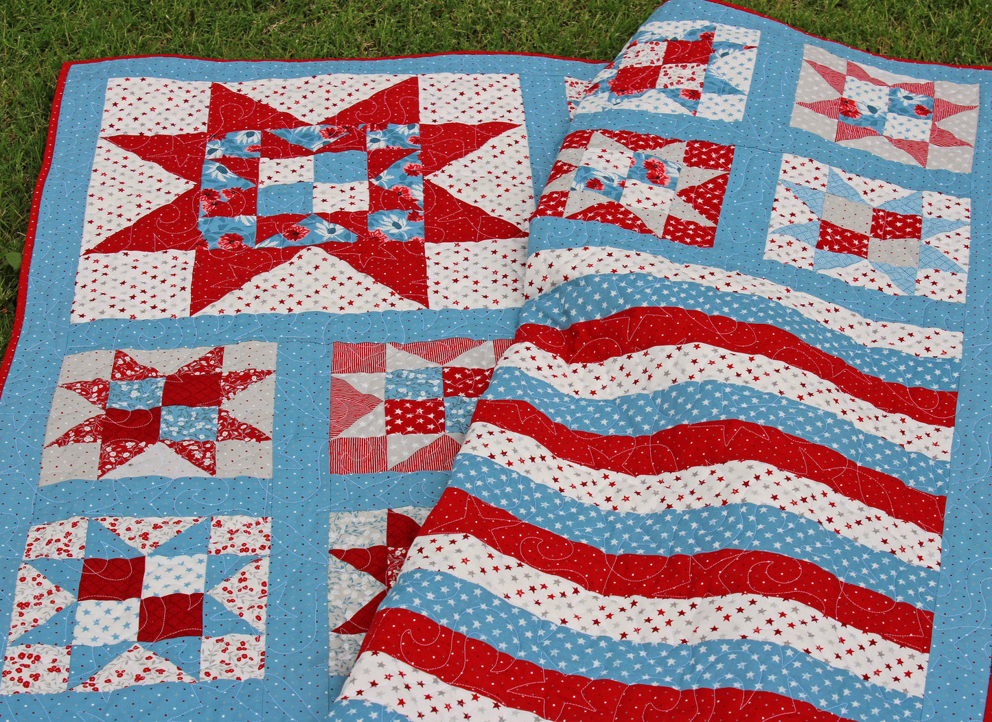 One Nation patriotic quilt pattern sample quilt with patchwork stars in three sizes and red white and blue stripes and blue sashing. Quilt is shown laying on the grass and folded over to show a close up of the large corner star.