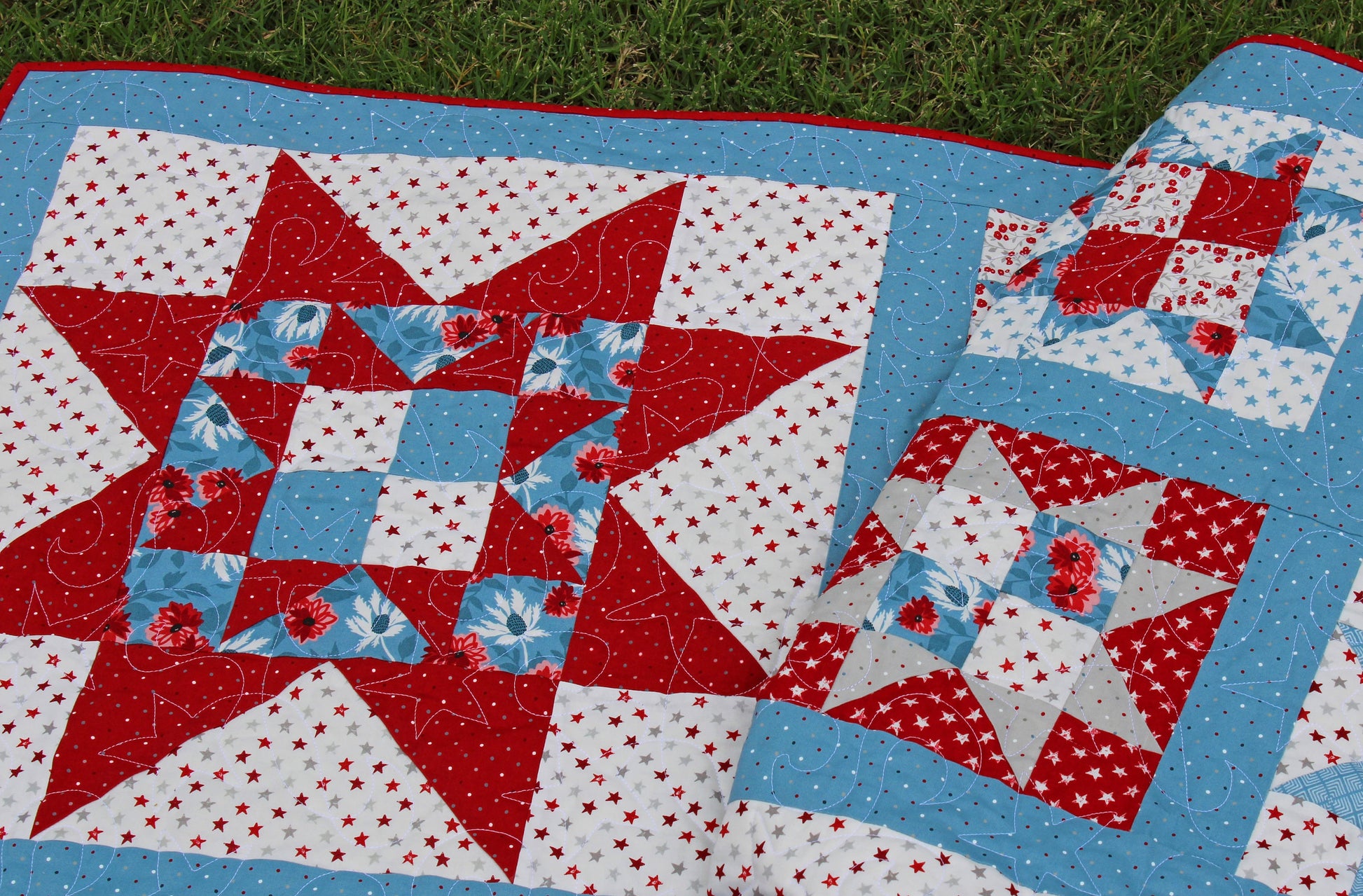 One Nation patriotic quilt pattern sample quilt with patchwork stars in three sizes and red white and blue stripes and blue sashing. Quilt is shown folded over with the detail of the large corner star showing.