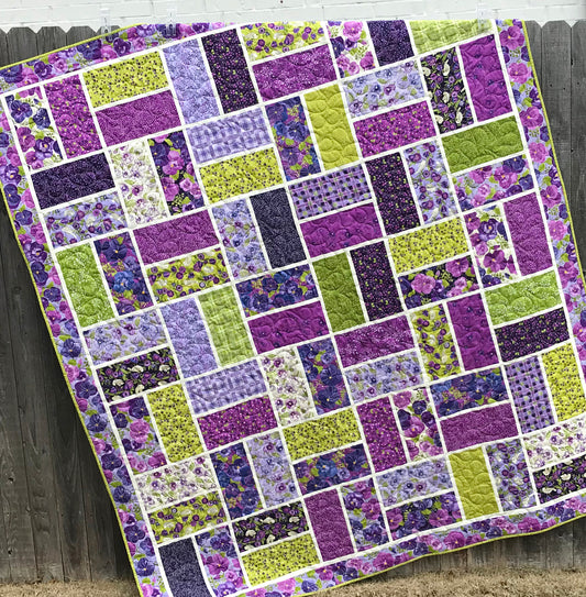 Bricktown sample quilt - purple and green large block quilt displayed hanging on a fence