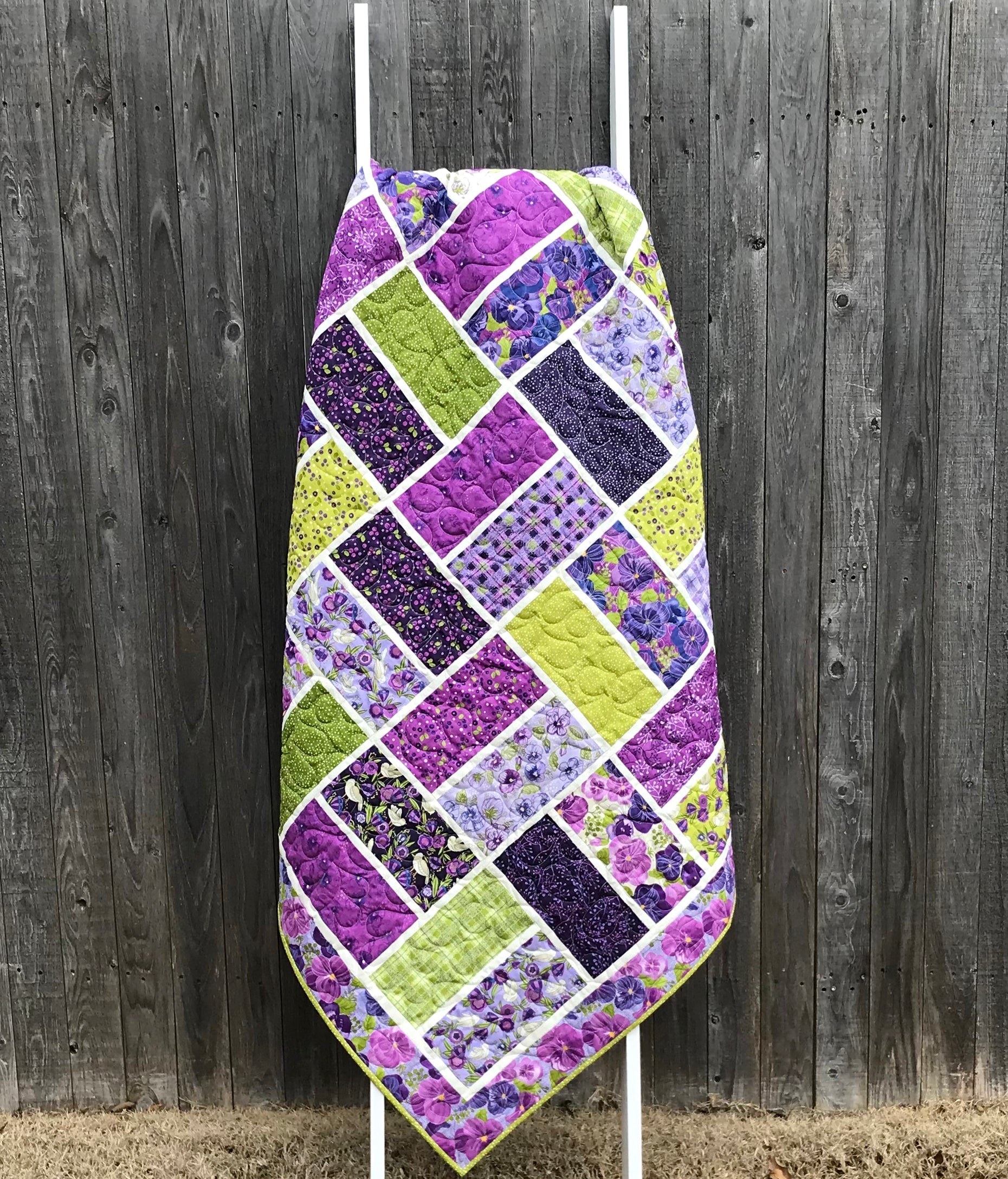 purple and green large block quilt displayed on a ladder against a fence