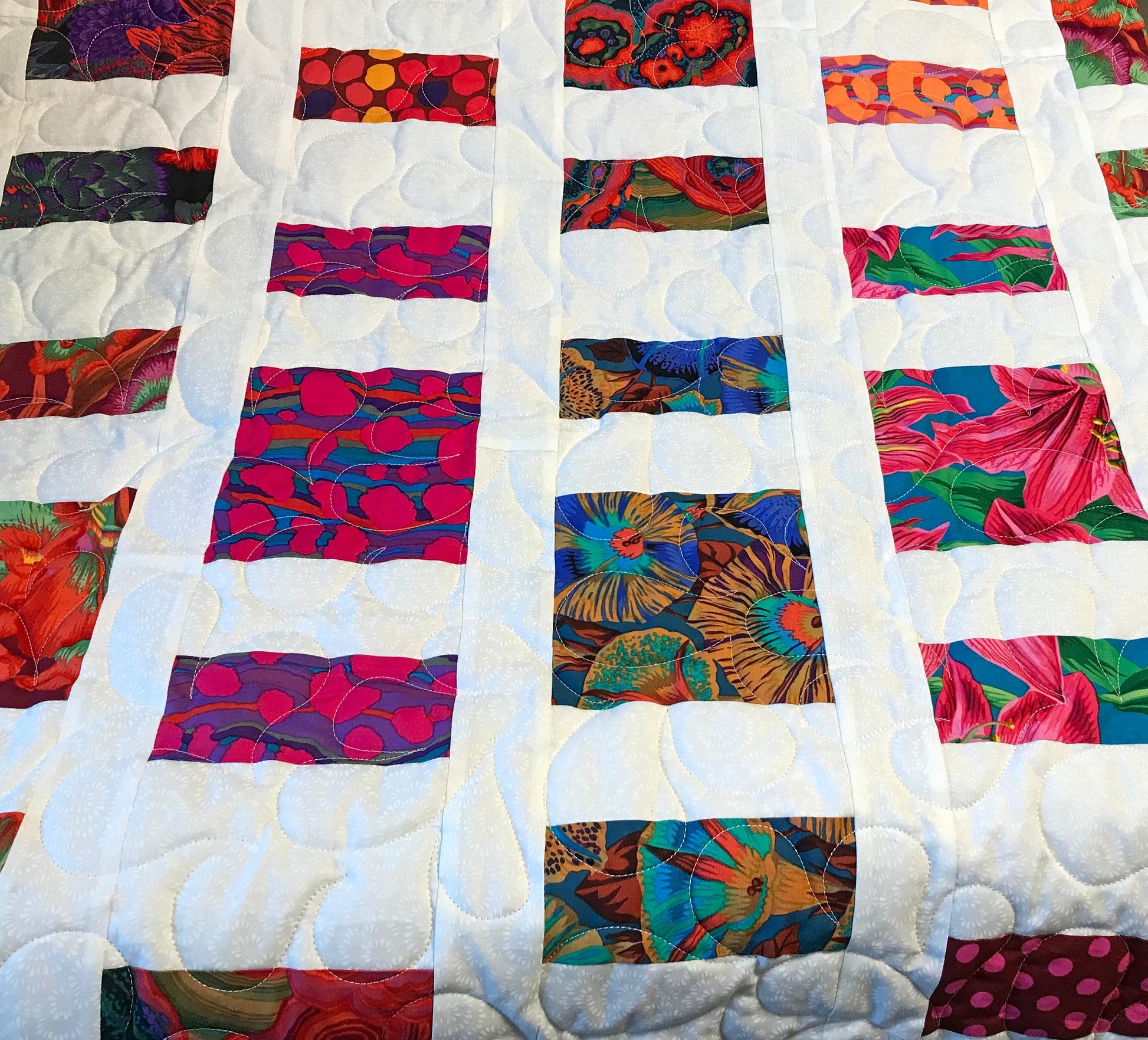 Close up of Quilt Pattern for charm squares that has nine columns of squares and rectangles of colorful Kaffe Fassett floral fabrics with white sashing between the columns. 