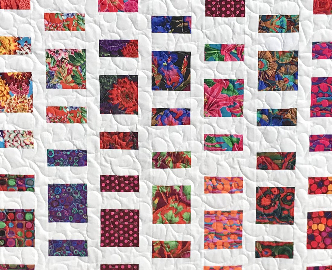 Close up of Quilt Pattern for charm squares that has nine columns of squares and rectangles of colorful Kaffe Fassett floral fabrics with white sashing between the columns. 