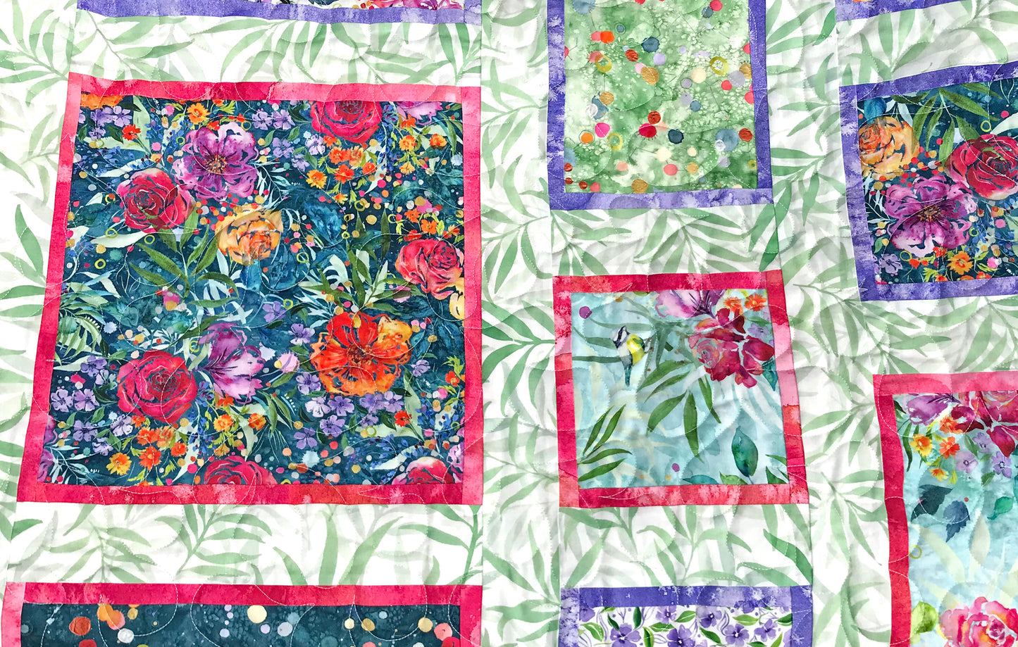 Close up of quilting on Handmade quilt featuring watercolor floral squares and rectangles framed with pink and purple fabric on a light green background. 