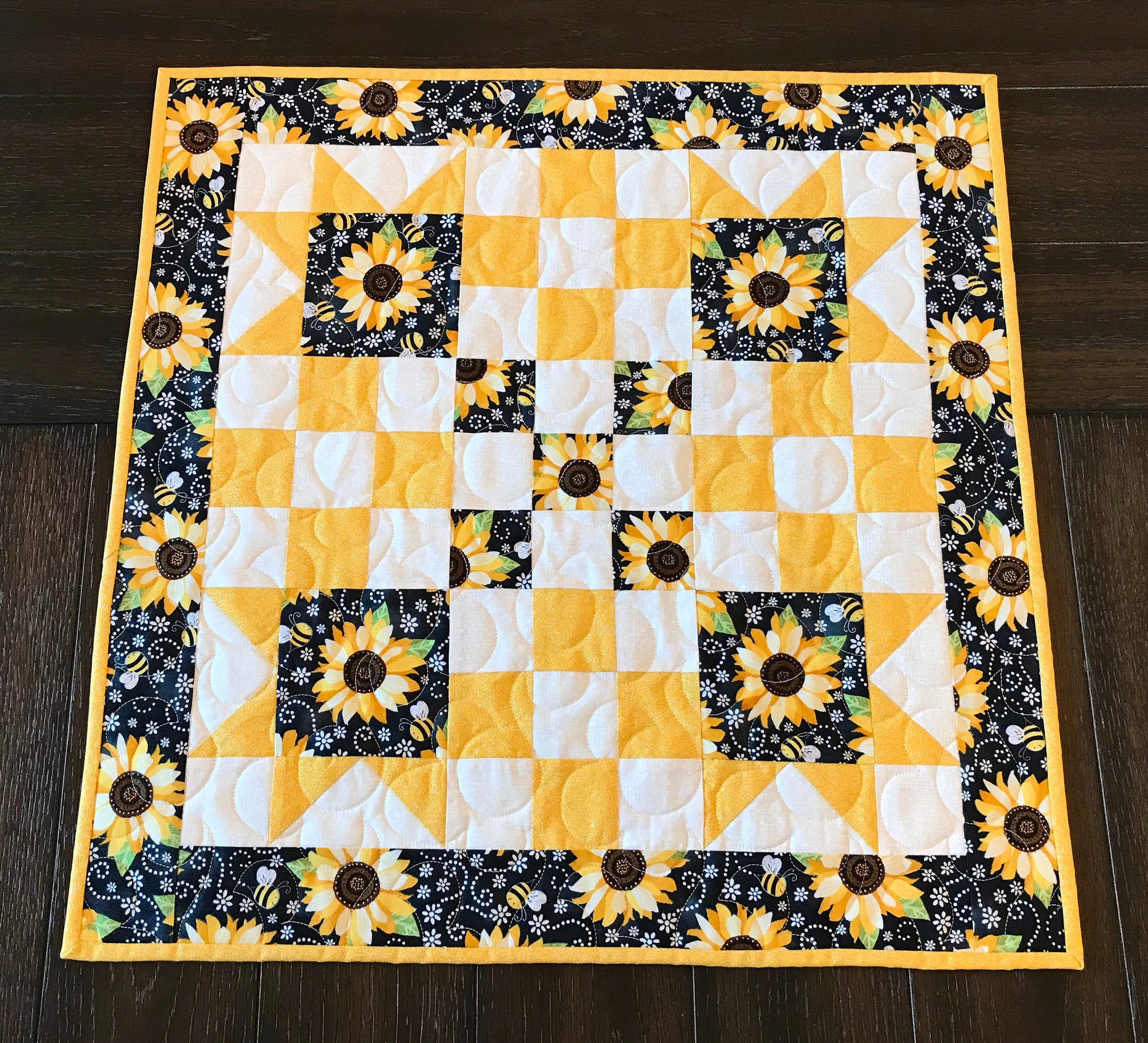 square topper displayed on a tale for pattern for a table runner or table topper that has sawtooth star corner units with nine patch blocks in between.