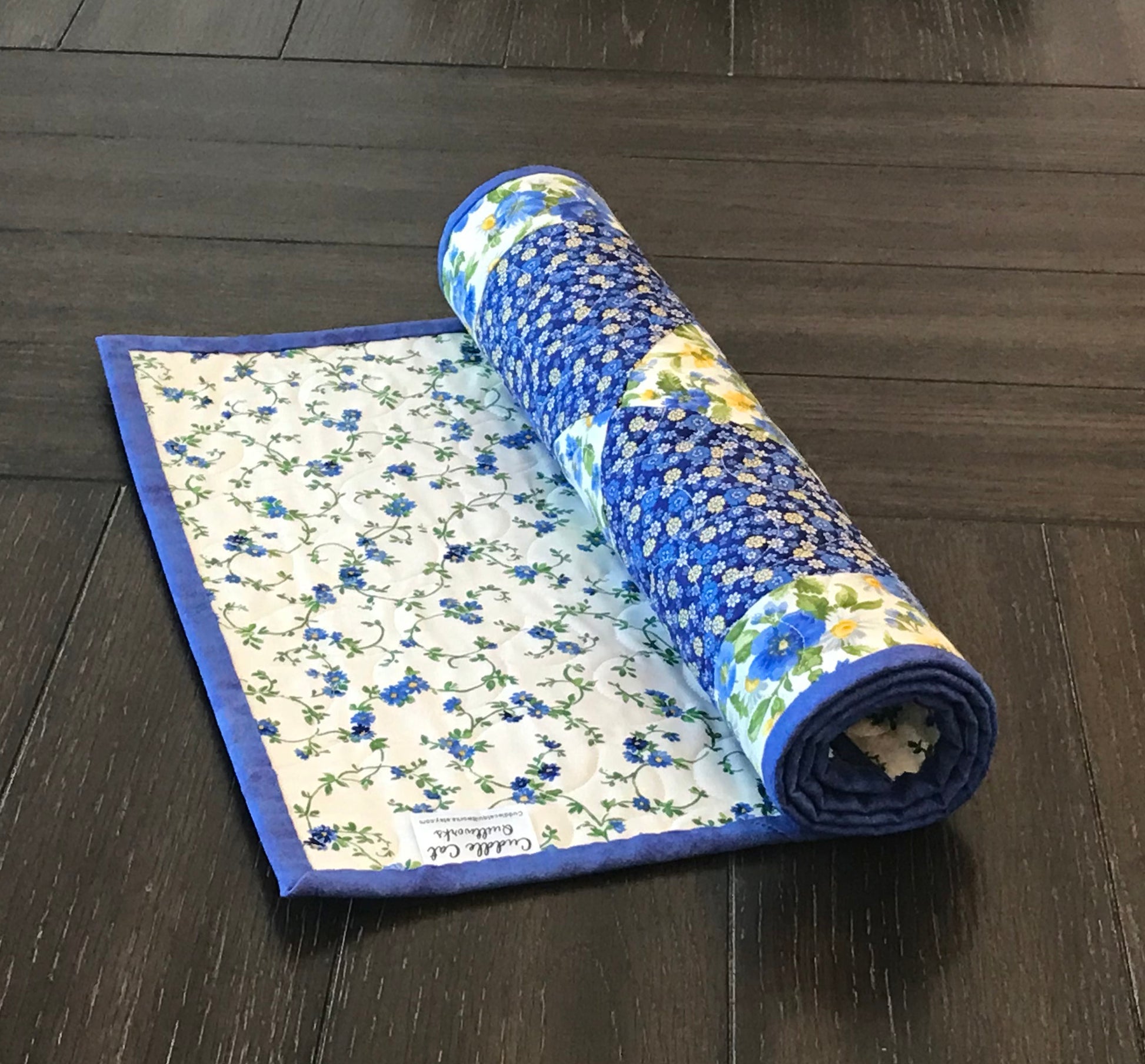 Blue and yellow floral table runner with a center diamond pattern displayed rolled up on a table