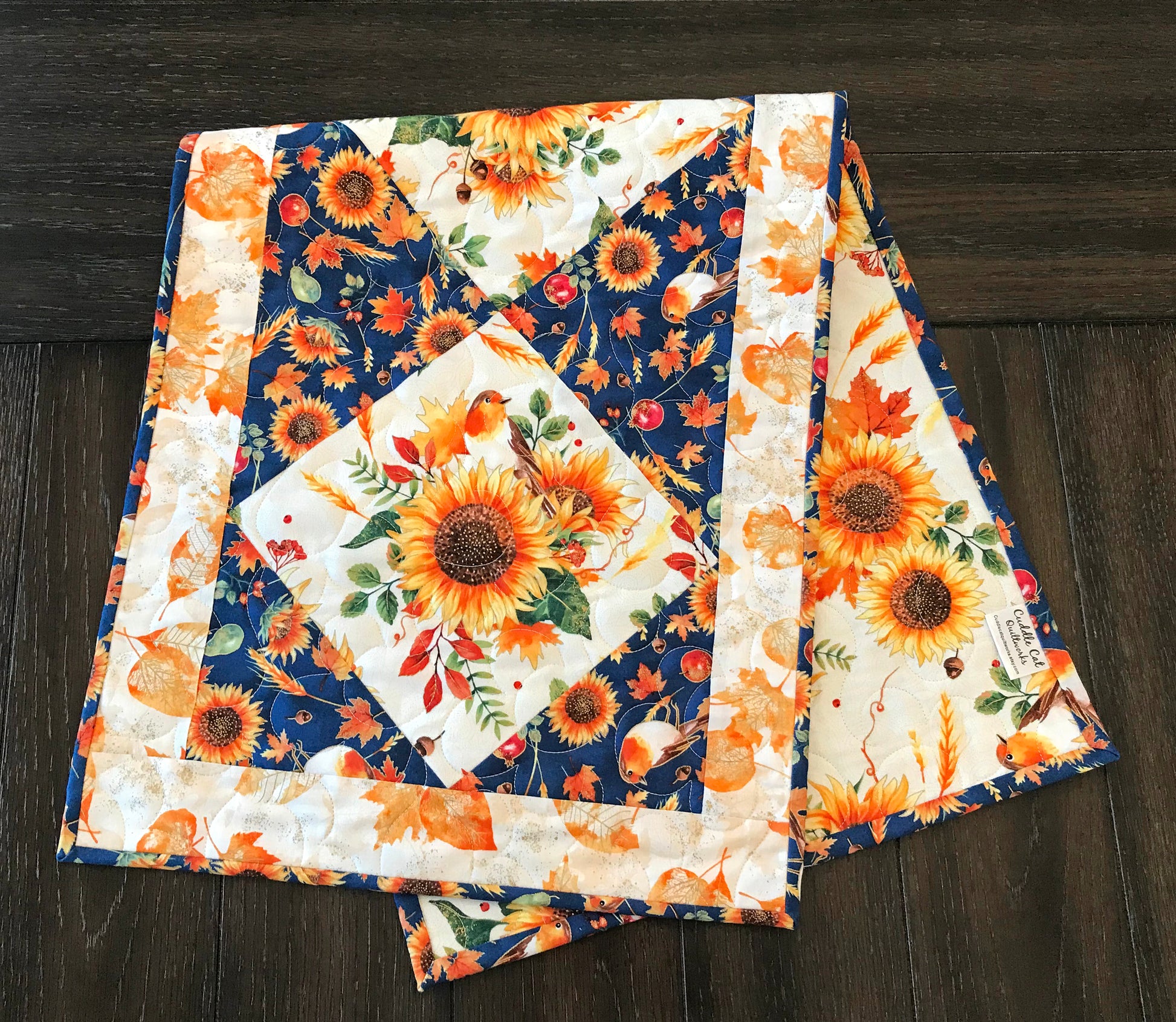 Sunflower themed fall table runner with a center diamond pattern of sunflowers surrounded by gold leaves and dark blue accents displayed on a table