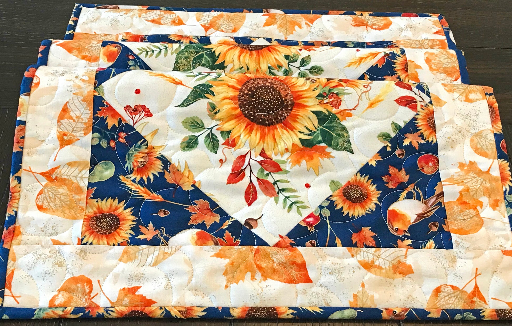 close up of Sunflower themed fall table runner with a center diamond pattern of sunflowers surrounded by gold leaves and dark blue accents displayed on a table