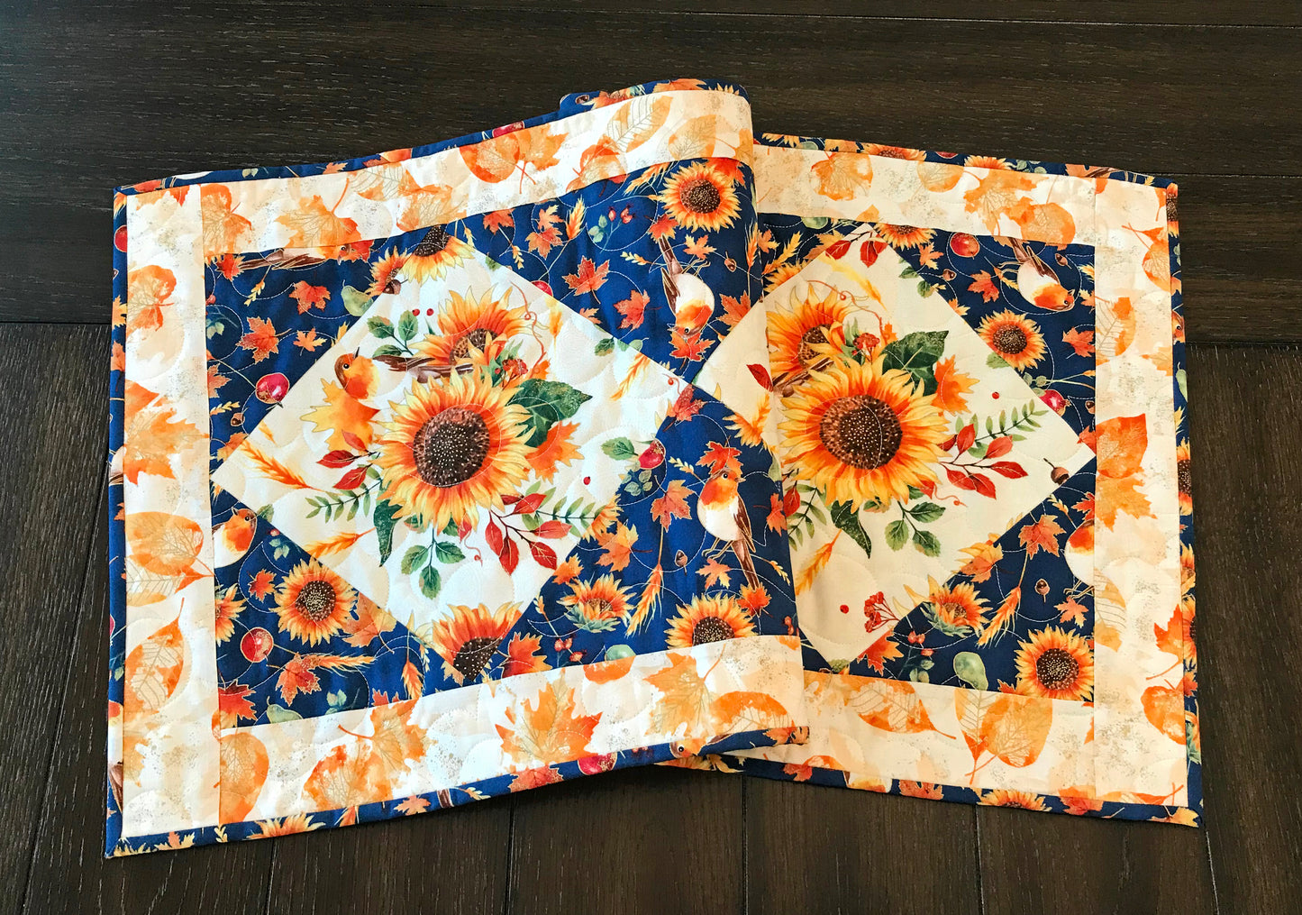 Sunflower themed fall table runner with a center diamond pattern of sunflowers surrounded by gold leaves and dark blue accents displayed on a table