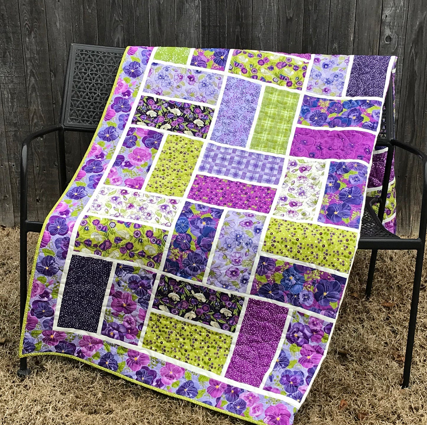 purple and green large block quilt displayed folded across a bench