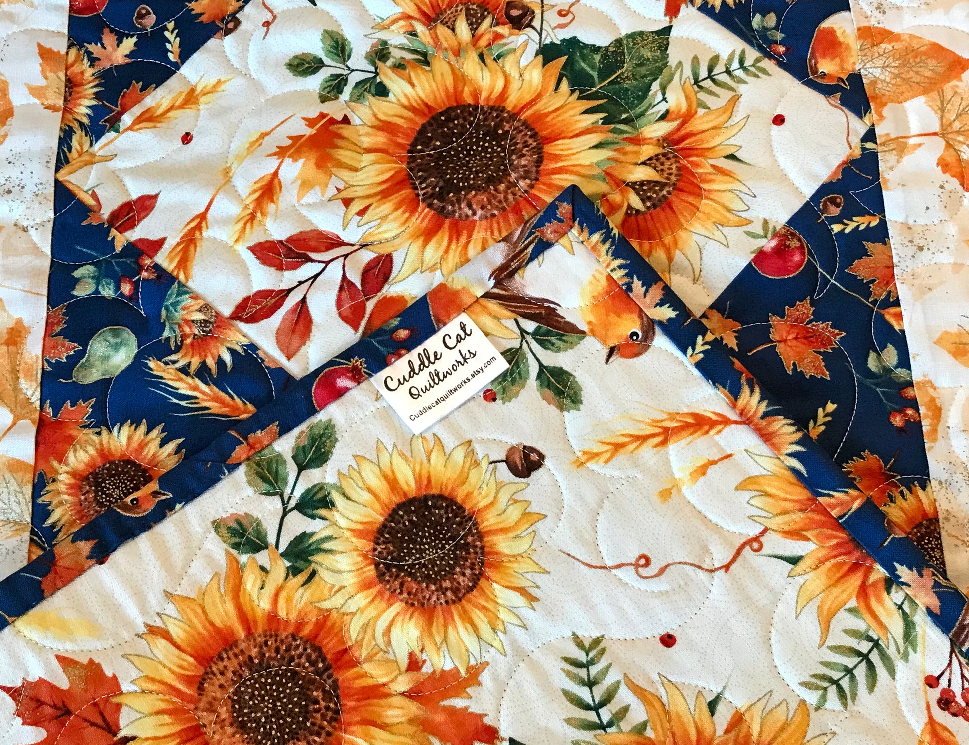 corner label close up of Sunflower themed fall table runner with a center diamond pattern of sunflowers surrounded by gold leaves and dark blue accents displayed on a table