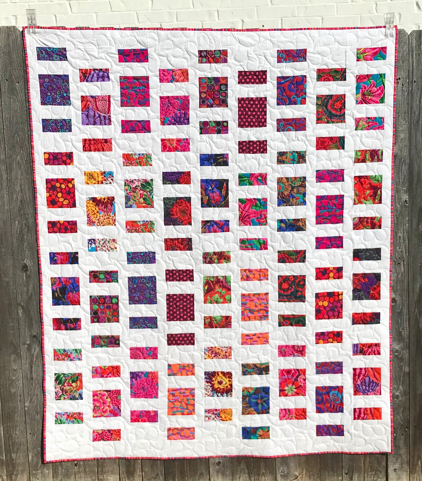 Quilt Pattern for charm squares that has nine columns of squares and rectangles with sashing between the columns. Quilt is displayed on a fence with colorful Kaffe Fassett fabrics.