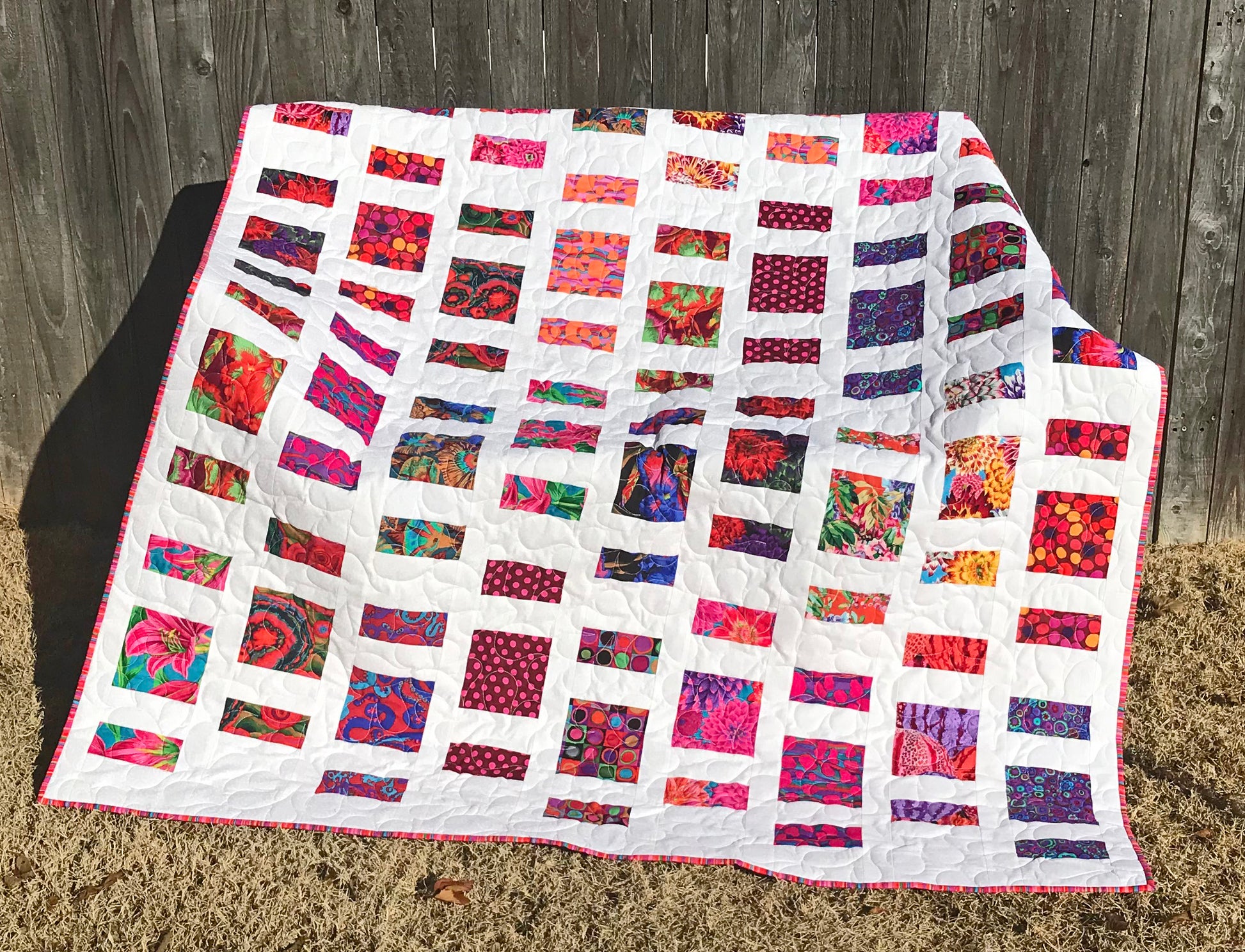 Quilt Pattern for charm squares that has nine columns of squares and rectangles with sashing between the columns. Quilt is displayed on a bench with colorful Kaffe Fassett fabrics.