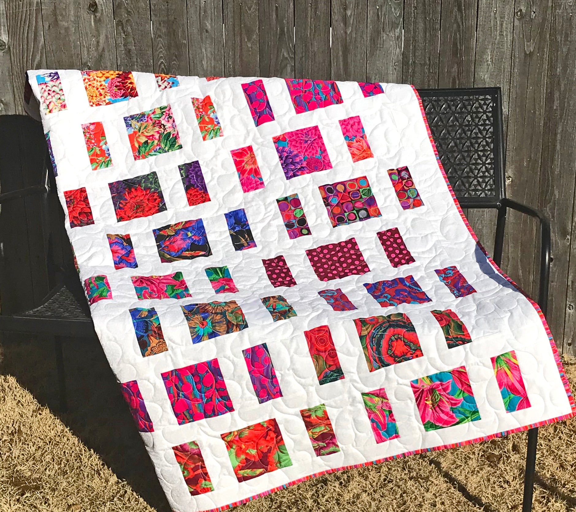 Quilt Pattern for charm squares that has nine columns of squares and rectangles with sashing between the columns. Quilt is displayed on a bench with colorful Kaffe Fassett fabrics.