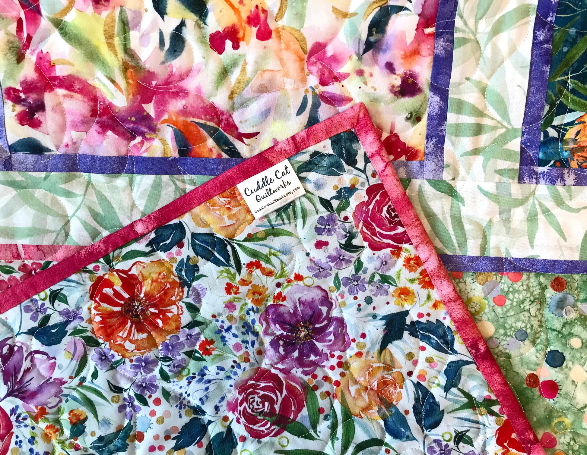 Close up of corner label on Handmade quilt featuring watercolor floral squares and rectangles framed with pink and purple fabric on a light green background.