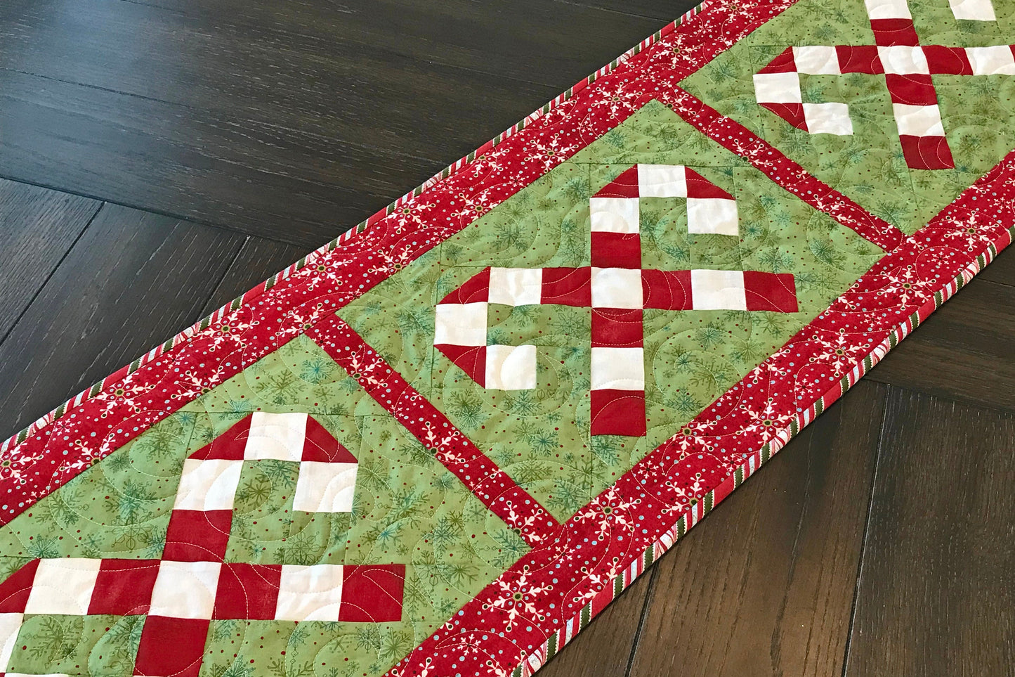 Digital pattern for a quilted Christmas table runner that has candy canes in three sections surrounded by a border.