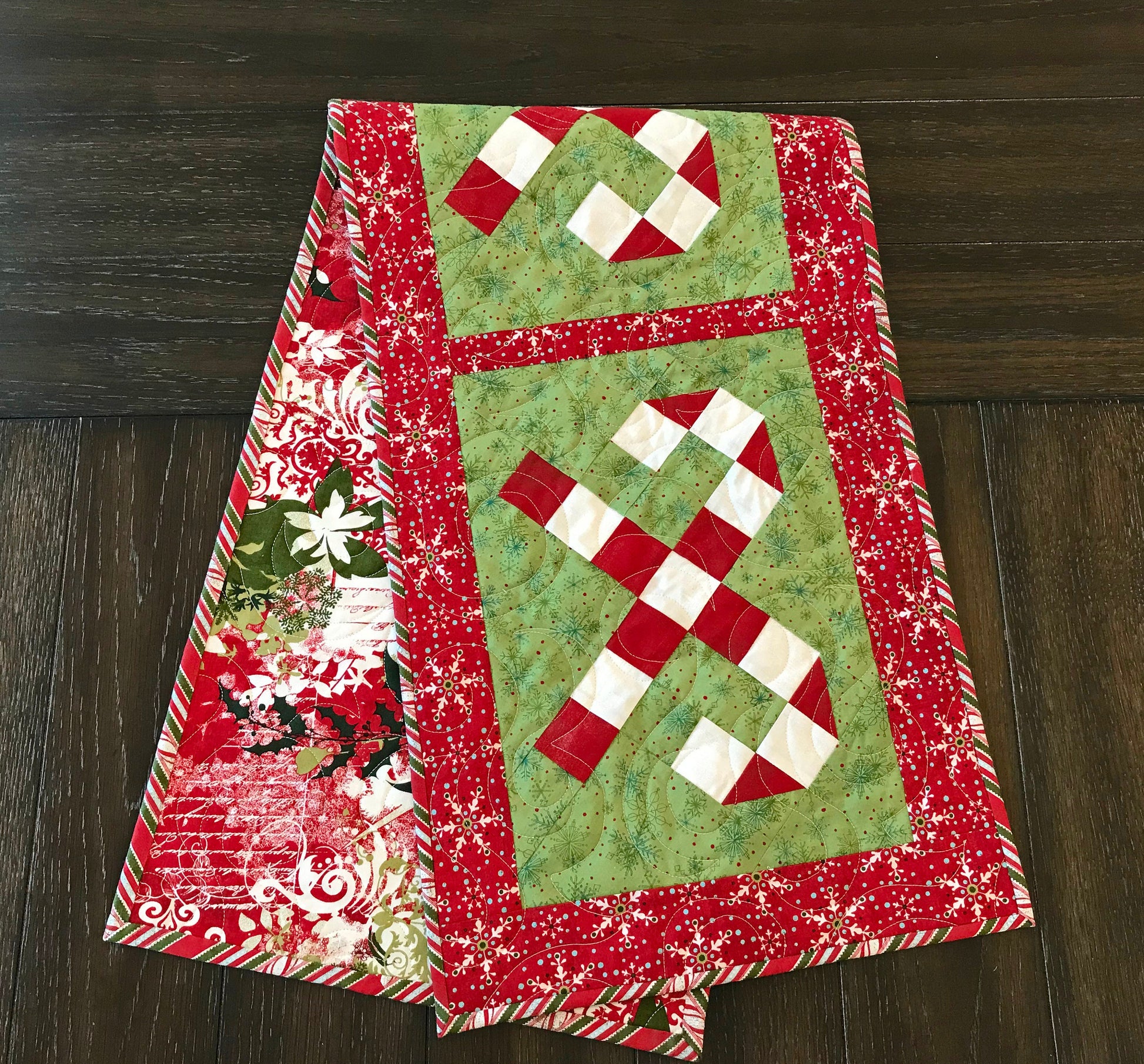 Digital pattern for a quilted Christmas table runner that has candy canes in three sections surrounded by a border.