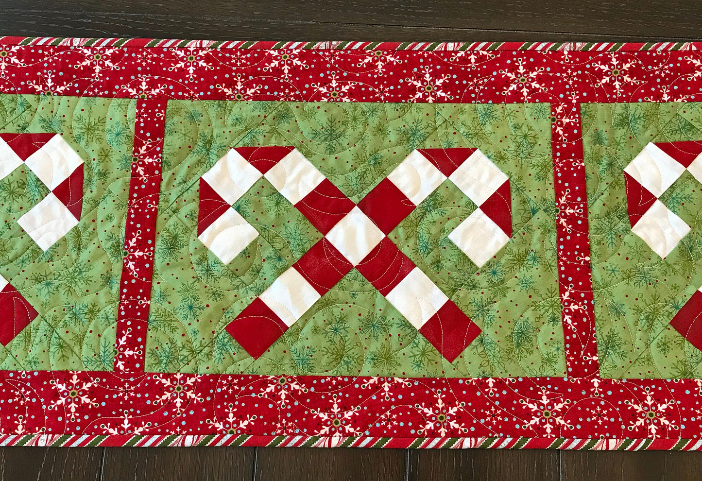 Digital pattern for a quilted Christmas table runner that has candy canes in three sections surrounded by a border.