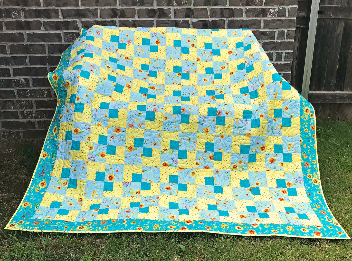 Cornerstones quilt pattern sample quilt. Four patch quilt in yellow and teal floral fabrics displayed on a bench.