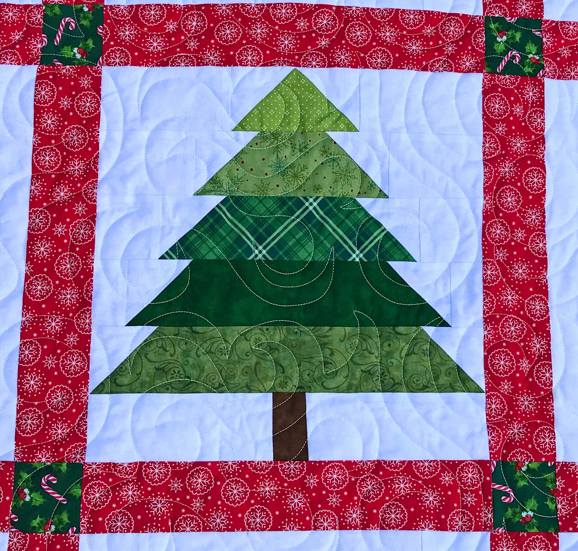 Christmastime quilt pattern with Christmas trees and ornament blocks surrounded by red sashing and a green holly border. Close up of Christmas tree block.