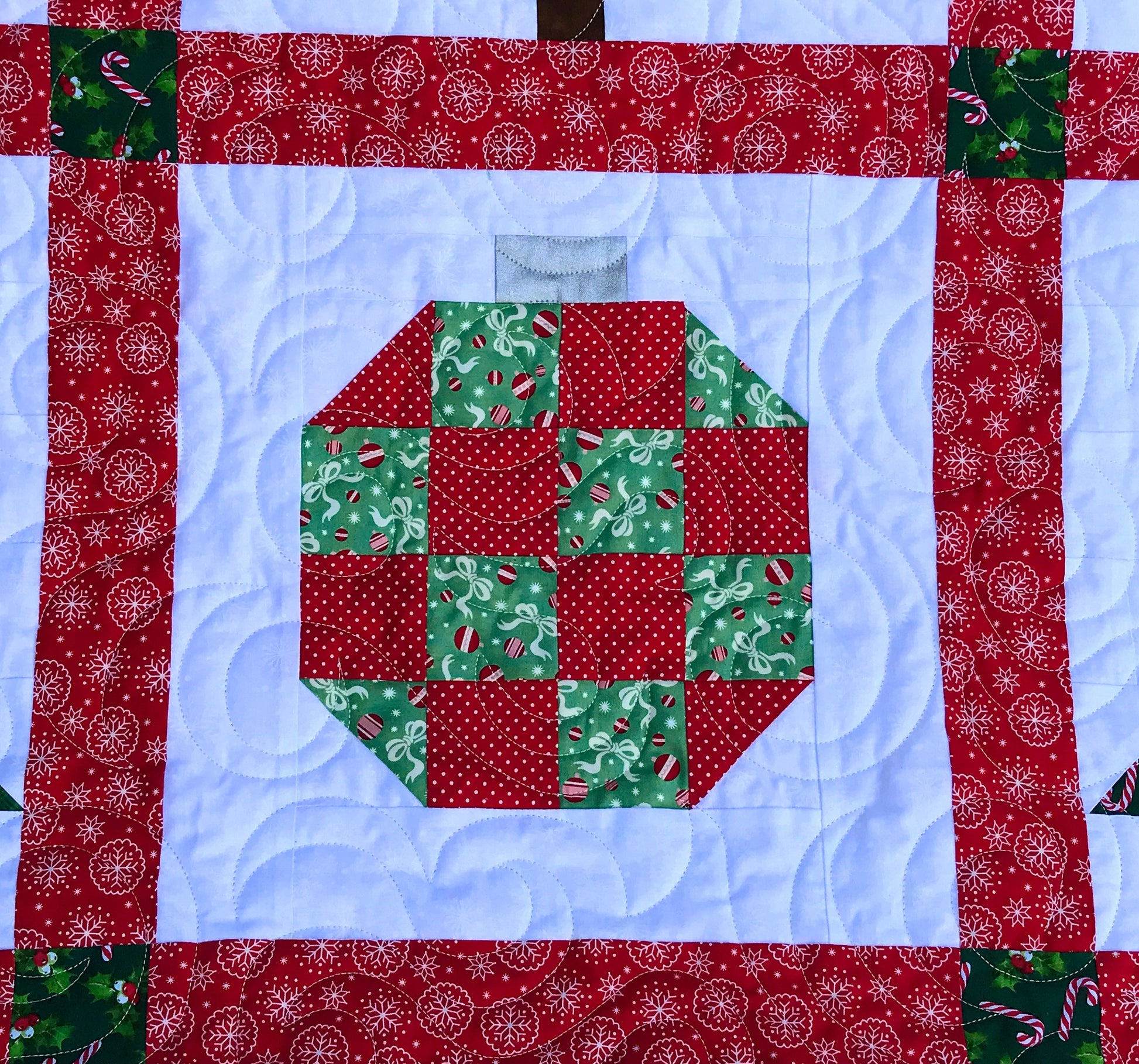 Christmastime quilt pattern with Christmas trees and ornament blocks surrounded by red sashing and a green holly border. Close up of ornament block.