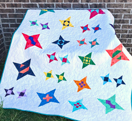 Star Gazing modern star sampler quilt pattern displayed on a bench. Stars are in various sizes with various fabrics on a white background.