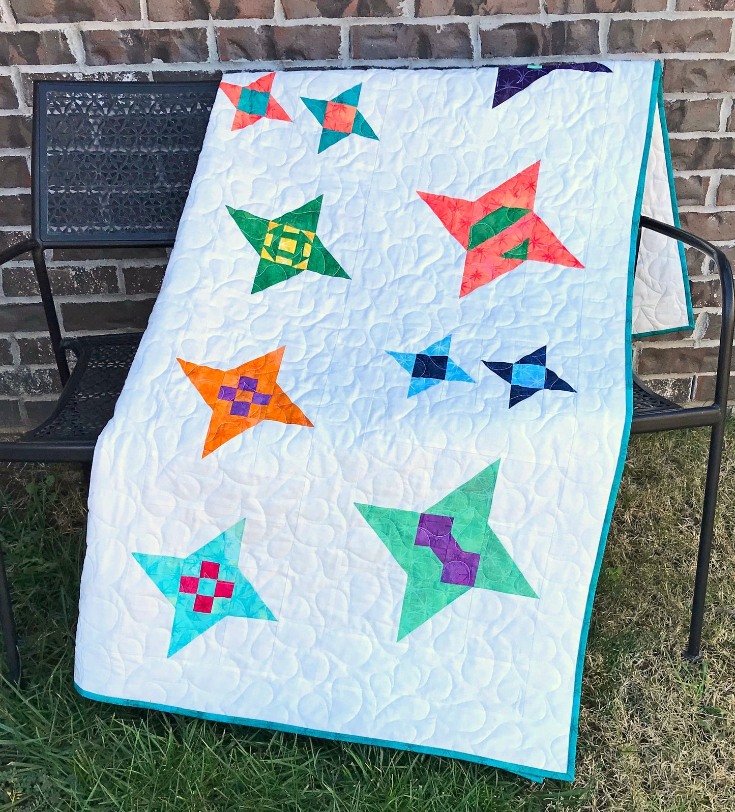 Star Gazing modern star sampler quilt pattern displayed on a bench. Stars are in various sizes with various fabrics on a white background.