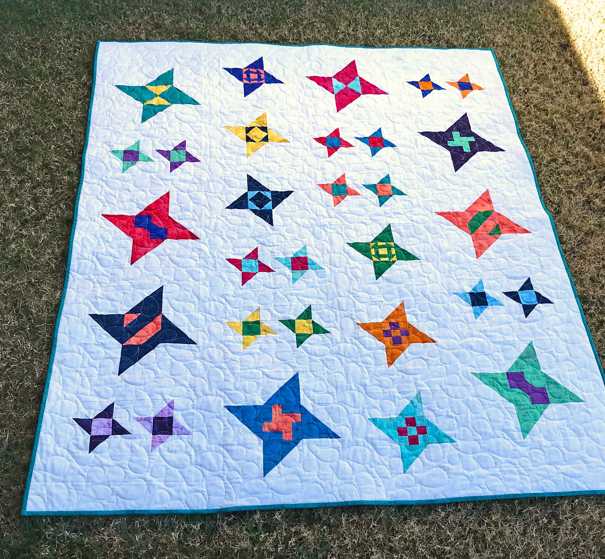 Star Gazing modern star sampler quilt pattern displayed on a lawn. Stars are in various sizes with various fabrics on a white background.