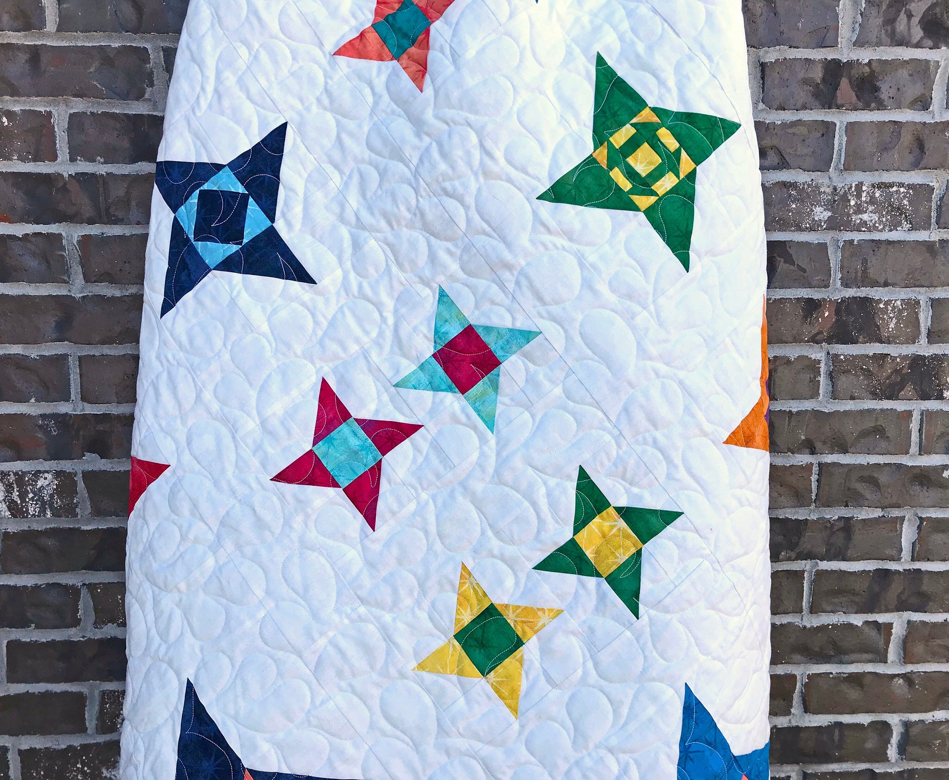 Star Gazing modern star sampler quilt pattern displayed on a ladder. Stars are in various sizes with various fabrics on a white background.